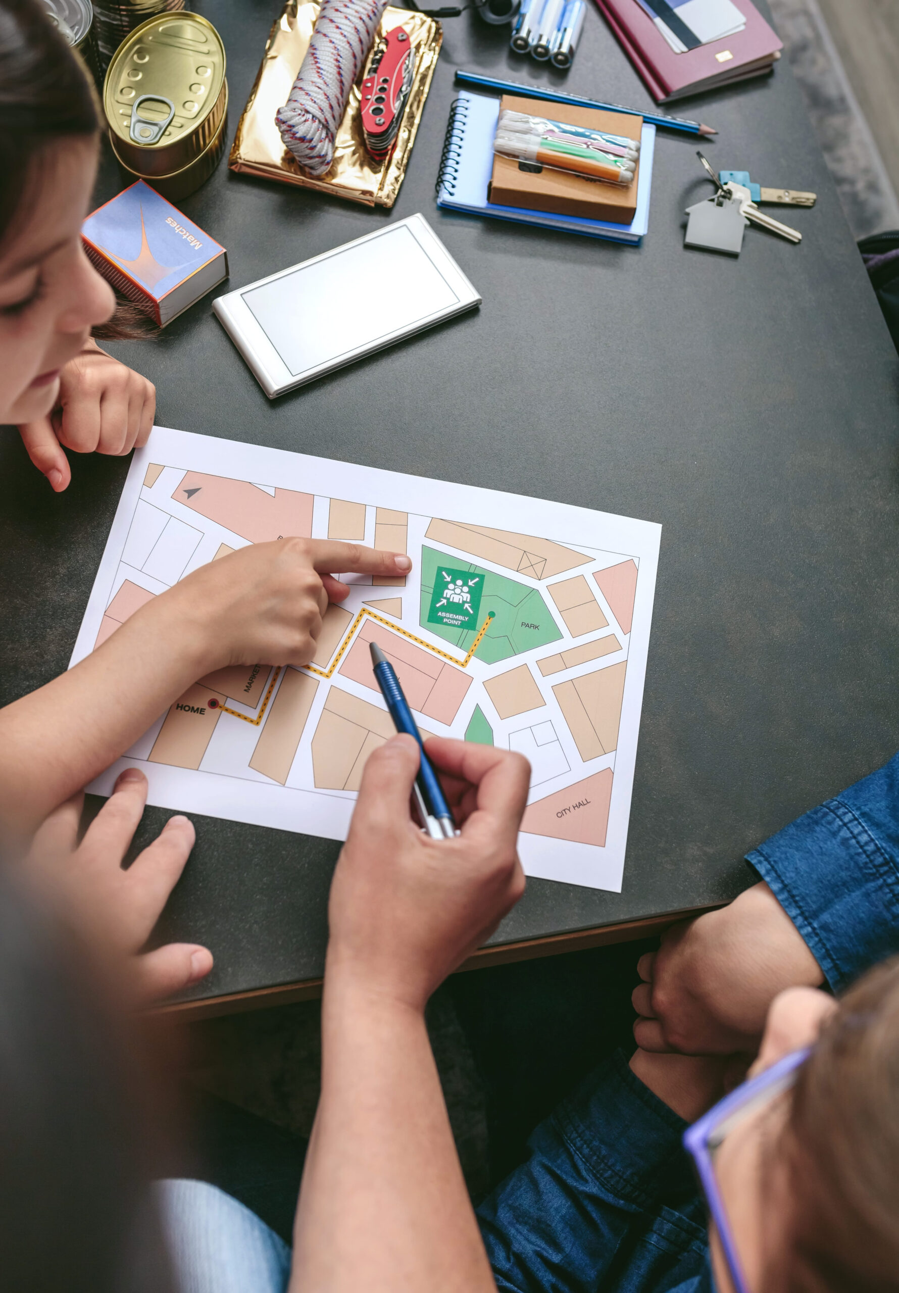 Top view of mother explaining to her children the assembly point map while preparing emergency backpacks